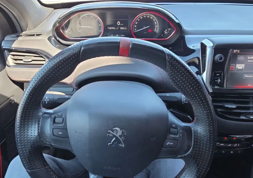 Vue intérieure centrée sur le volant sport en cuir perforé avec bande rouge de la Peugeot 208 GTI noire de 2015.