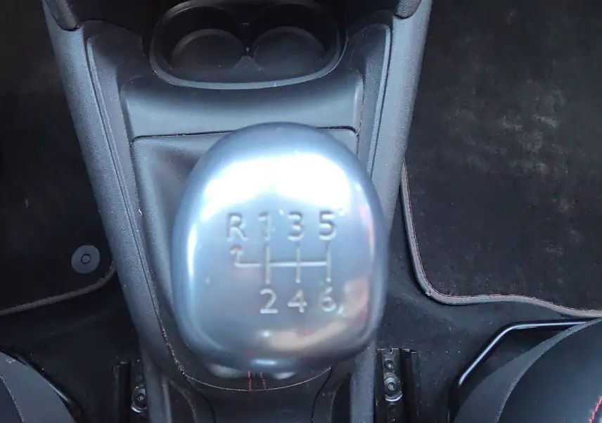 Gros plan sur le levier de vitesses manuel argenté de la Peugeot 208 GTI noire, entouré de tapis noirs et sièges sport.