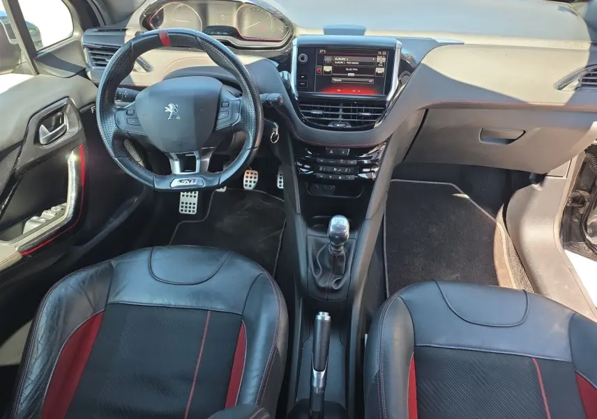 Vue intérieure frontale de la Peugeot 208 GTI 2015 noire, avec volant sport GTI, sellerie cuir/alcantara et écran tactile central.