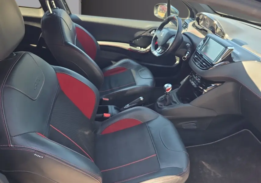Vue intérieure côté conducteur de la Peugeot 208 GTI 2015, sièges baquets cuir noir et rouge, volant sport et tableau de bord moderne.