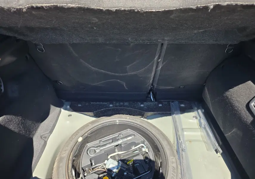 Coffre ouvert vu de dessus d'une Peugeot 208 GTI noire, montrant la roue de secours et les outils de bord.