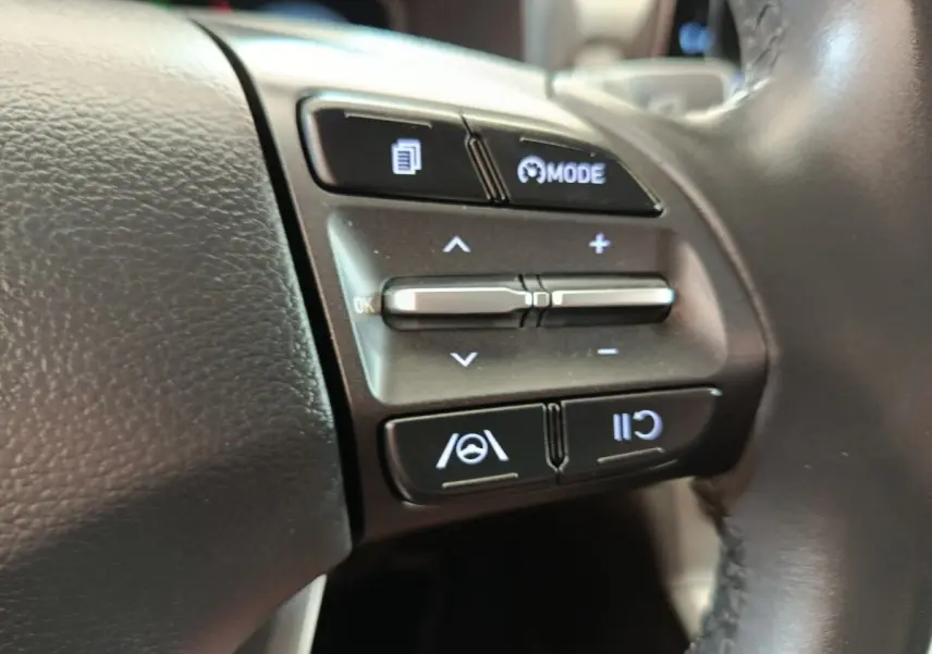 Gros plan sur les commandes du volant cuir noir du Hyundai Kona électrique 2023, boutons de régulateur adaptatif et assistance au maintien de voie.