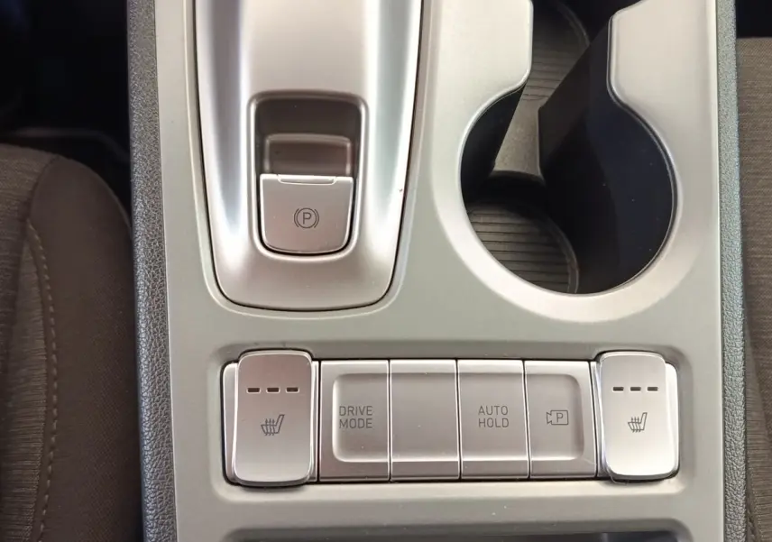 Vue rapprochée de la console centrale argentée du Hyundai Kona électrique 2023, avec boutons de chauffage sièges et frein à main électrique.