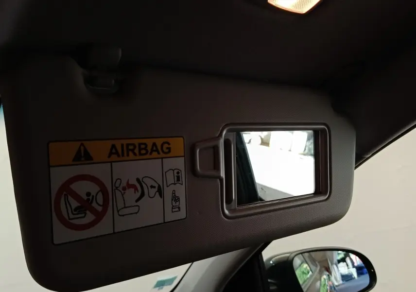 Miroir de pare-soleil côté conducteur avec avertissement airbag, vue intérieure du toit et rétroviseur latéral noir visible.