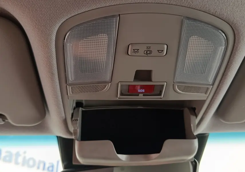 Vue intérieure du plafonnier gris clair avec éclairages, bouton SOS rouge et compartiment lunettes ouvert dans une Hyundai Kona électrique noire.