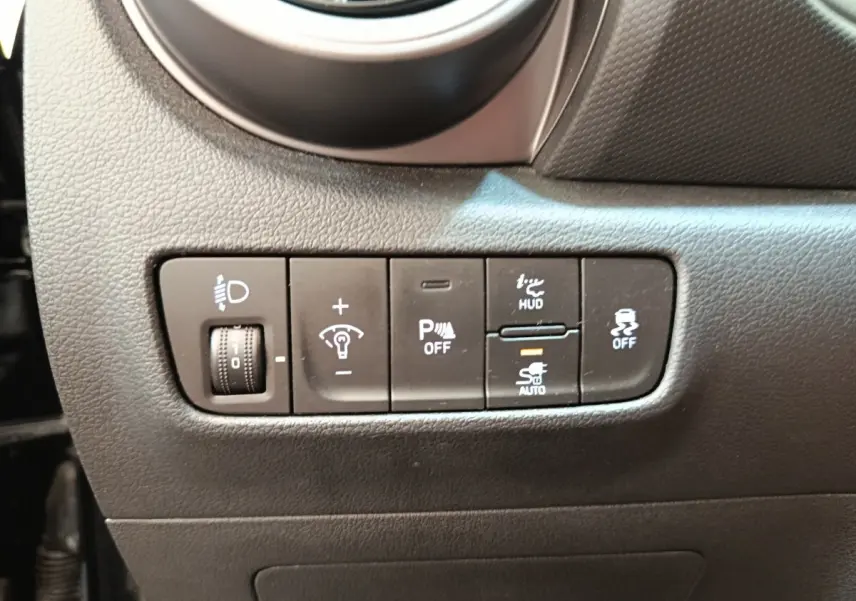 Gros plan sur les commandes de réglage des phares et aides à la conduite du tableau de bord d'une Hyundai Kona noire 2023.