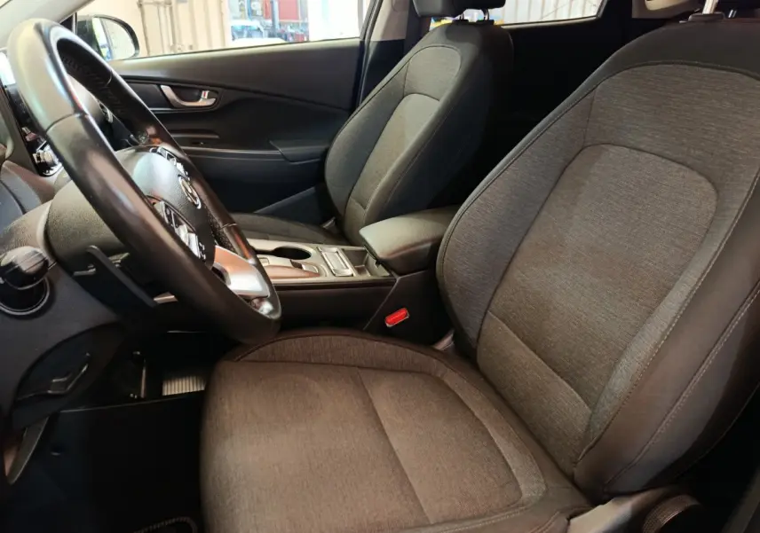 Intérieur avant droit du Hyundai Kona électrique 2023, sièges tissu gris et volant cuir multifonctions.