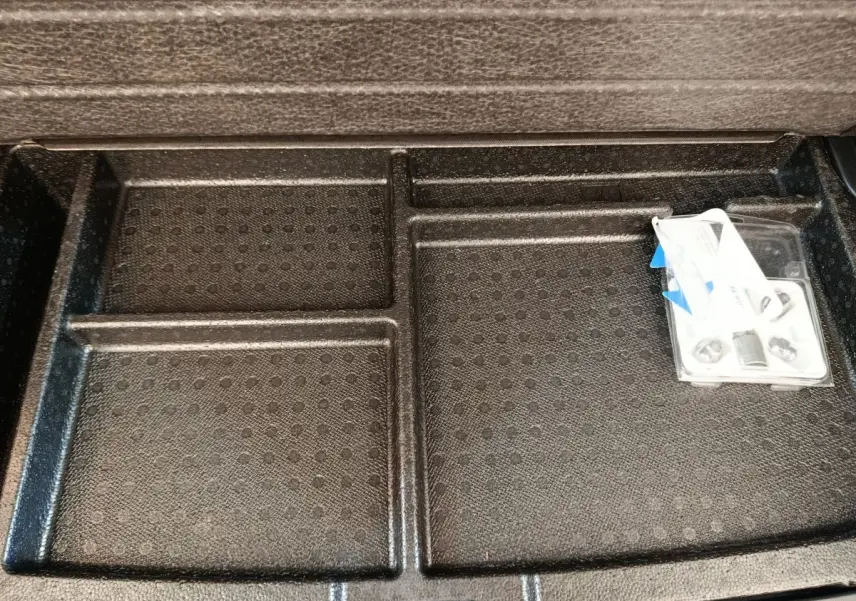 Rangement sous plancher de coffre noir du Hyundai Kona électrique 2023 avec compartiments et accessoires visibles.