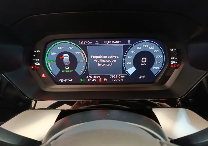 Vue rapprochée du tableau de bord numérique de l'Audi A3 hybride blanche, affichant les compteurs et alertes de conduite.