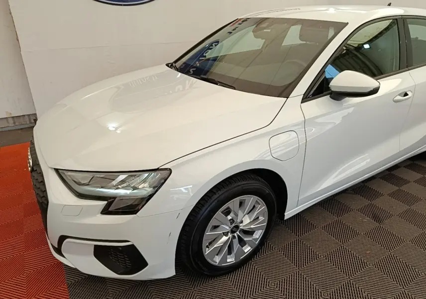 Audi A3 40 TFSI e blanc en 3/4 avant droit, avec prises de recharge et phares LED visibles.