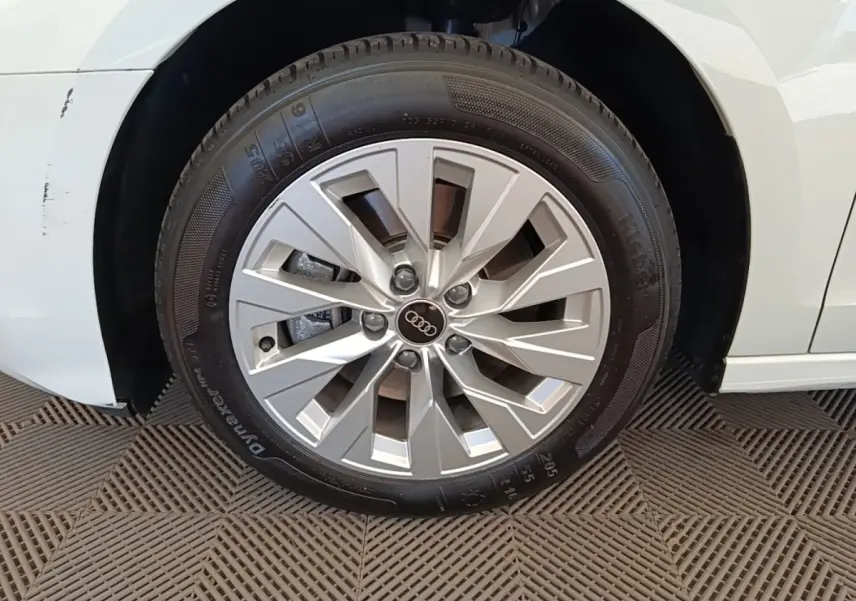 Gros plan sur la roue avant gauche d’une Audi A3 blanche, mettant en valeur la jante en alliage et le logo Audi central.