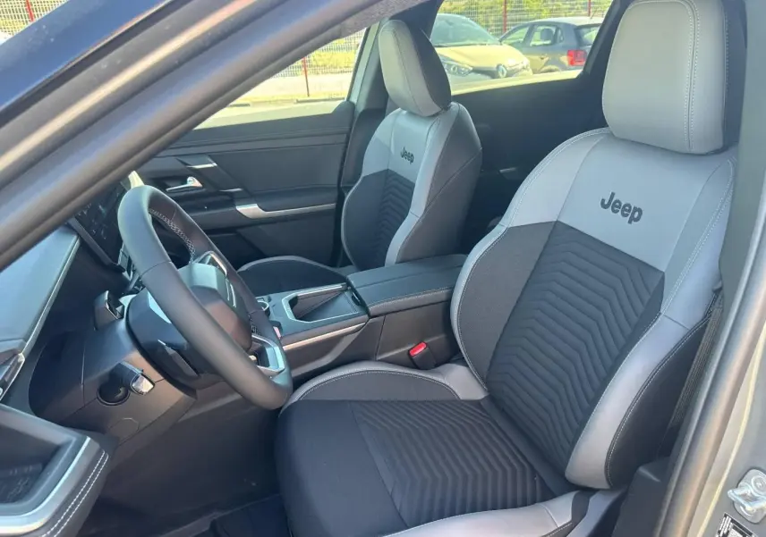 Vue intérieure côté conducteur du Jeep Compass 2026, sièges bi-ton gris et noir avec logo Jeep brodé.