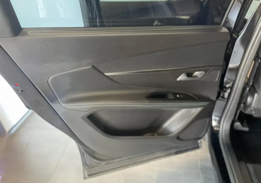 Gros plan sur la porte arrière gauche noire métallisée du Peugeot 5008 2024 avec insert carbone et poignée grise.