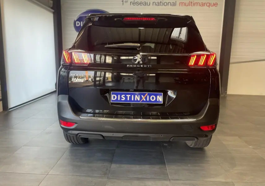 Vue arrière d'un Peugeot 5008 noir métallisé avec feux arrière LED 3D et logo Peugeot visible en intérieur showroom.