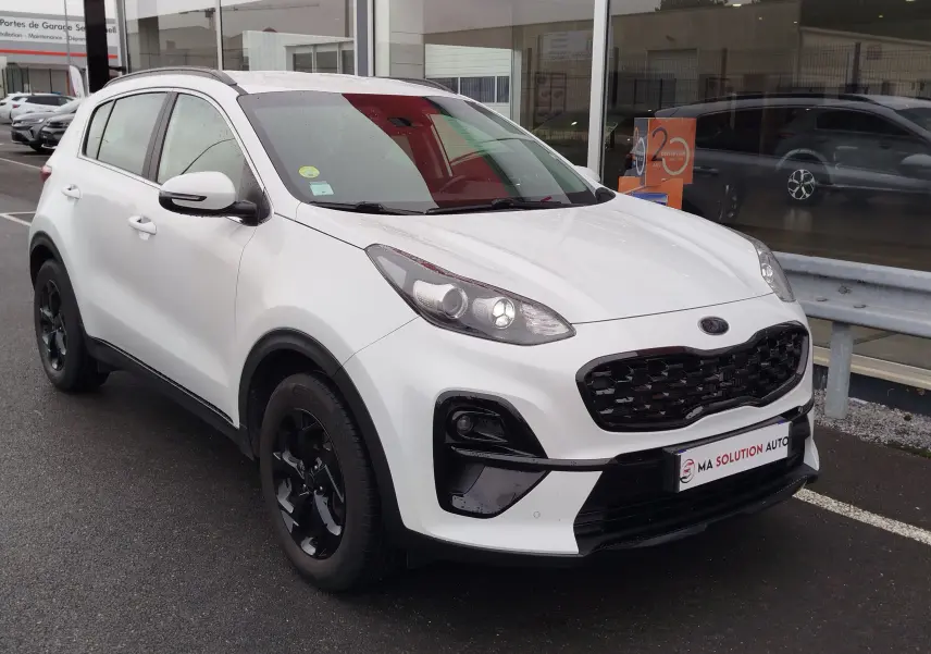 KIA Sportage blanc vue 3/4 avant droit avec calandre noire et jantes noires, stationné devant un showroom.