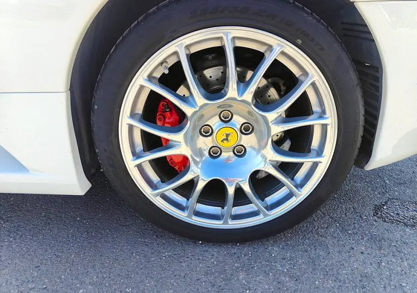 Gros plan sur la roue avant gauche d'une Ferrari F430 Spider blanche avec étrier de frein rouge et jante argentée brillante.
