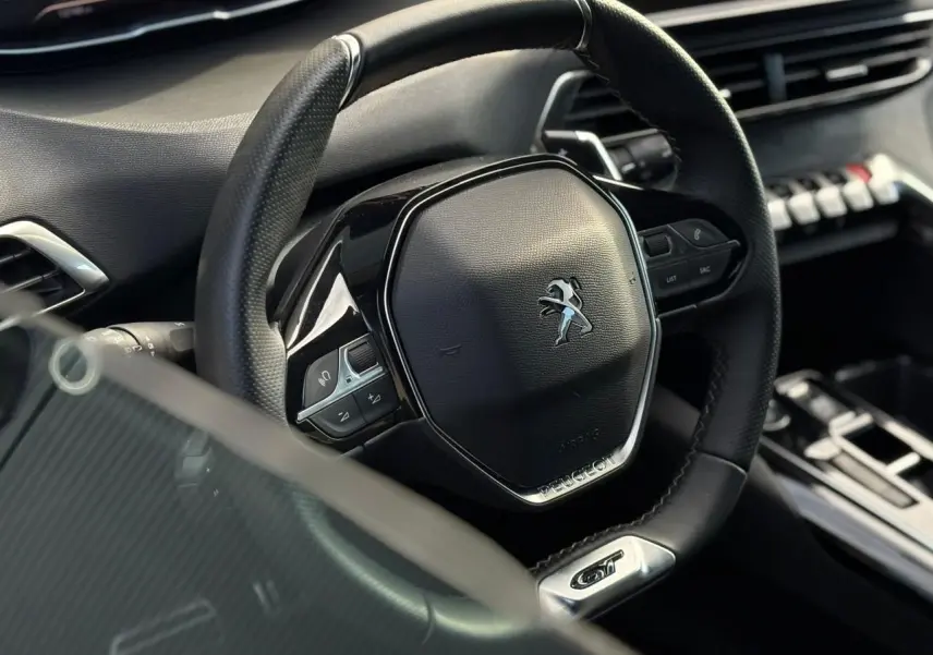 Gros plan sur le volant cuir perforé noir avec logo Peugeot et badge GT dans l’habitacle du 3008 2023.