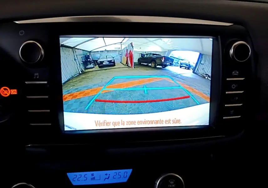 Écran tactile intérieur montrant la caméra de recul d'une Toyota Yaris blanche, avec lignes de guidage colorées.