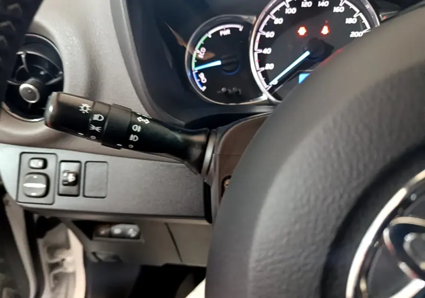 Vue rapprochée du tableau de bord et du commodo gauche de la Toyota Yaris hybride blanche, avec compteurs éclairés.