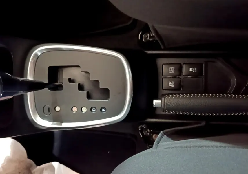 Vue rapprochée de la console centrale de la Toyota Yaris blanche, montrant la boîte automatique et le frein à main cuir noir.