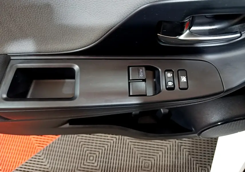 Gros plan sur la commande de lève-vitre et verrouillage sur la portière avant gauche d'une Toyota Yaris blanche.