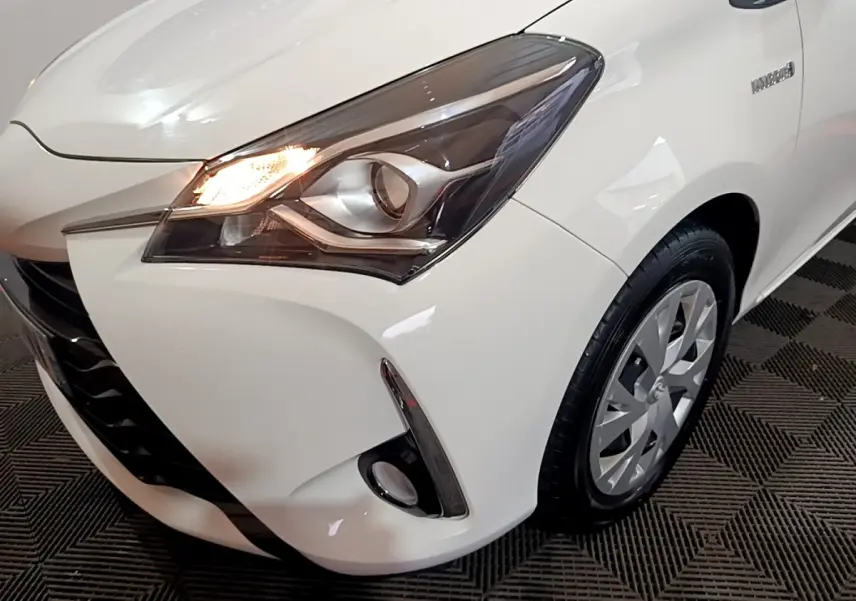 Gros plan sur l'avant droit blanc d'une Toyota Yaris 2019 avec phare allumé et antibrouillard visible.