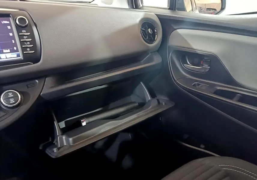 Intérieur côté passager d'une Toyota Yaris blanche 2019, boîte à gants ouverte et tableau de bord avec écran tactile visible.