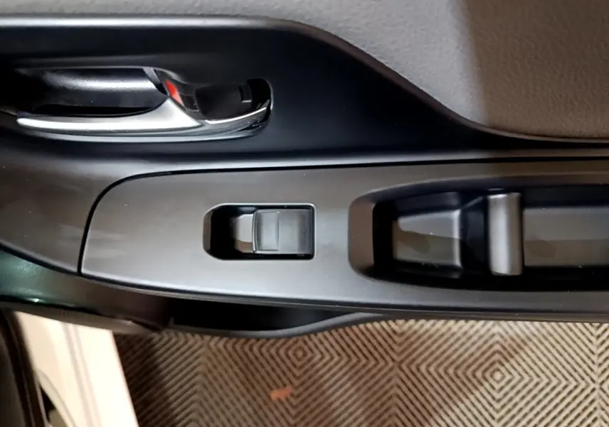 Gros plan sur la poignée intérieure et les commandes de la porte côté conducteur d'une Toyota Yaris blanche.