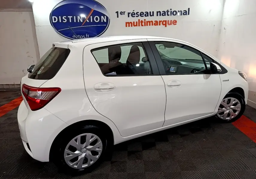 Profil droit de la Toyota Yaris hybride blanche 2019 en intérieur, avec jantes acier et logo Distinxion en arrière-plan.