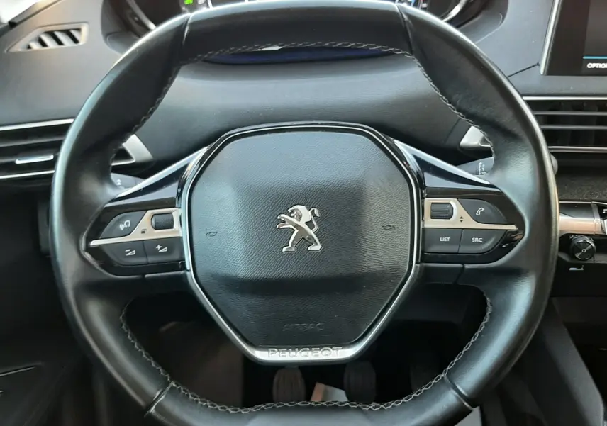 Vue rapprochée du volant noir en cuir du Peugeot 3008 2019, avec commandes intégrées et tableau de bord numérique en arrière-plan.