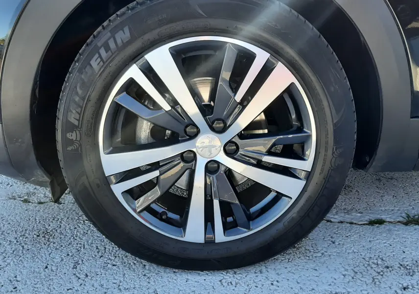 Gros plan sur la roue avant gauche noire d’un Peugeot 3008 2019 avec jante alliage bicolore et pneu Michelin.