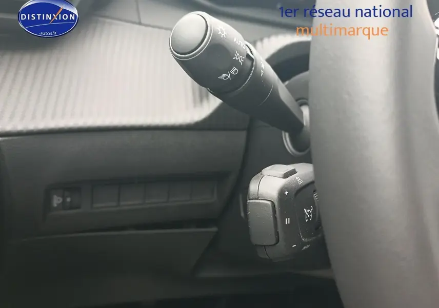 Gros plan sur la commande des phares et régulateur de vitesse derrière le volant d’un Peugeot 2008 rouge elixir.