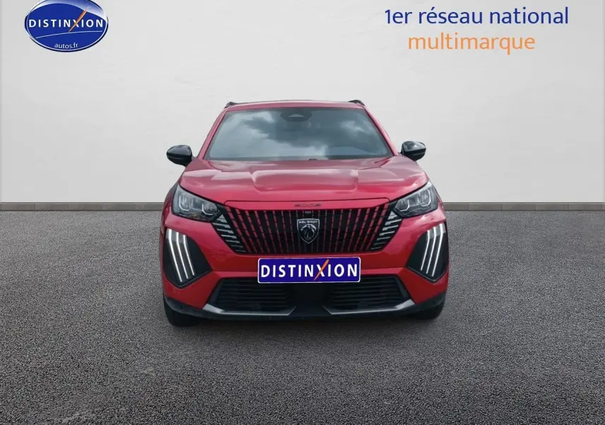 Vue frontale d'un Peugeot 2008 rouge elixir avec calandre noire et feux LED verticaux allumés.