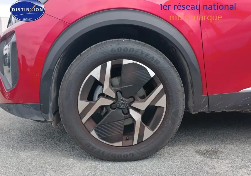 Gros plan sur la roue avant gauche avec jante alu du Peugeot 2008 rouge elixir, montrant le passage de roue noir.