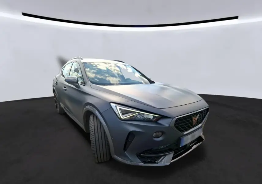 Vue 3/4 avant gauche d'une CUPRA Formentor 1.4 E-HYBRID 2024 en gris foncé mat avec phares LED distinctifs.