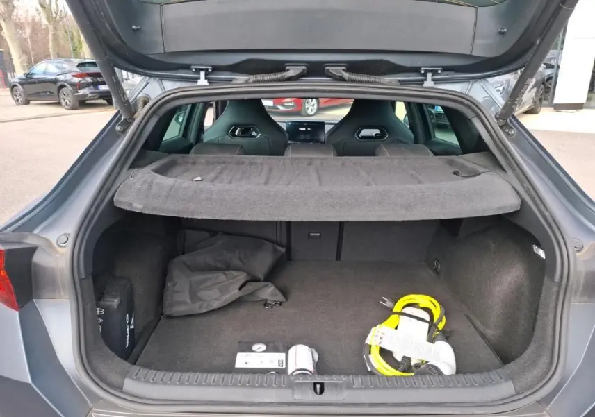 Coffre ouvert d’une CUPRA Formentor gris foncé mat, vue arrière montrant l’espace de chargement avec câble de recharge jaune.
