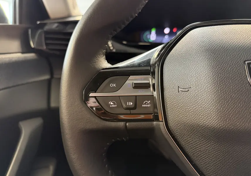 Gros plan sur la partie gauche du volant noir de la Peugeot 308 Hybrid 145, avec commandes de limitation et assistance.