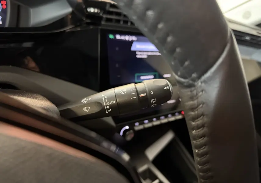Gros plan sur la commande d’essuie-glace côté gauche du volant dans l’habitacle d’une Peugeot 308 Hybrid 145 bleu obsession.