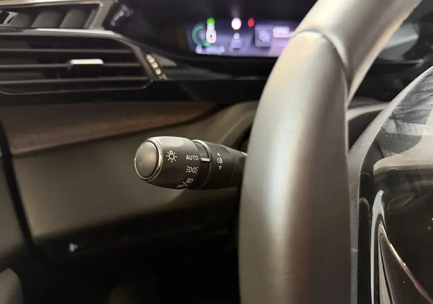 Gros plan sur la commande des phares à gauche du volant dans l’habitacle sombre d’une Peugeot 308 Hybrid 2025.