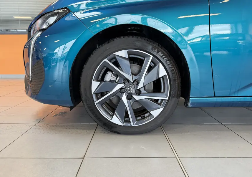 Gros plan sur la roue avant gauche et la partie avant bleue Obsession d'une Peugeot 308 Hybrid 145 e-DCS6 Allure 2025.