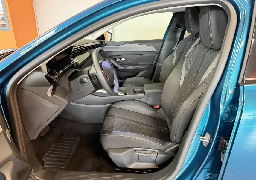 Vue intérieure côté conducteur de la Peugeot 308 Hybrid 145 Allure bleu obsession, sièges tri-matières et tableau de bord moderne.