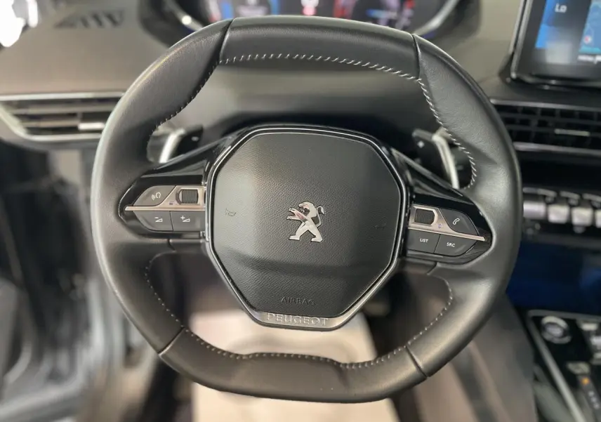 Volant compact en cuir noir du Peugeot 5008 2024 avec commandes intégrées et logo lion central visible.