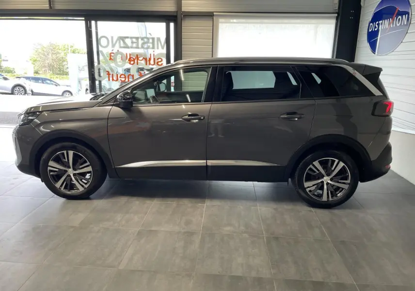 Profil droit du Peugeot 5008 gris platinium 2024 en showroom, avec jantes alliage bi-ton et vitres surteintées.