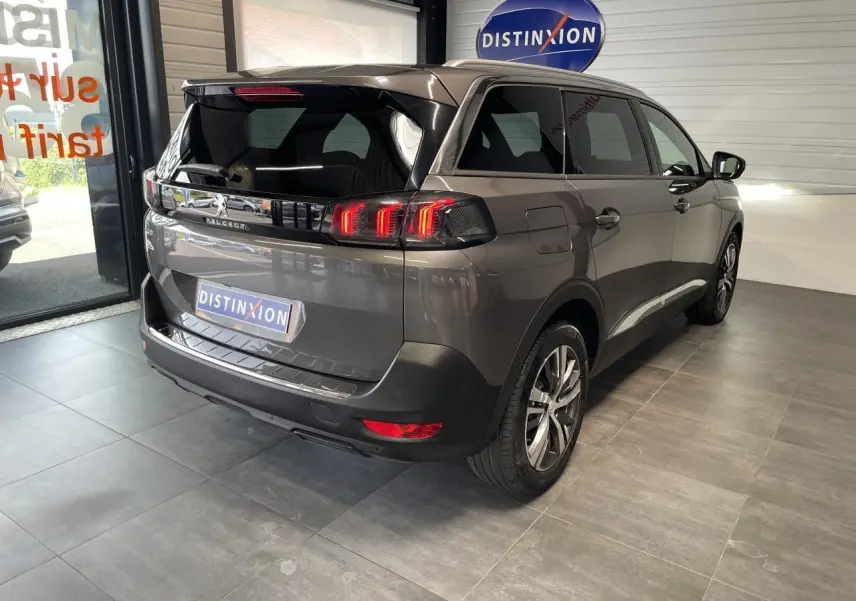 Vue 3/4 arrière droit du Peugeot 5008 gris platinium avec feux LED 3D et vitres arrière surteintées en showroom.