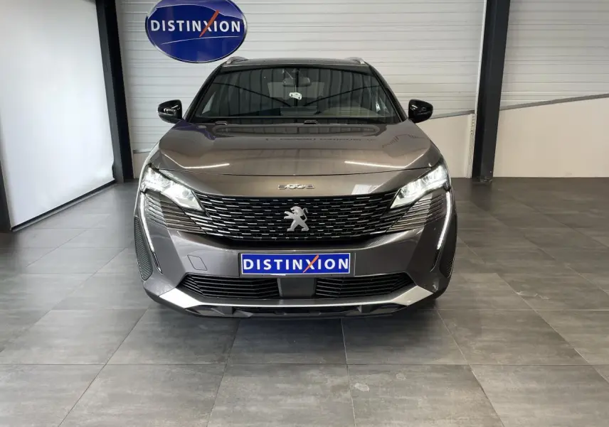 Vue frontale d'un Peugeot 5008 gris platinium avec calandre à damier chromé et feux LED allumés en showroom.