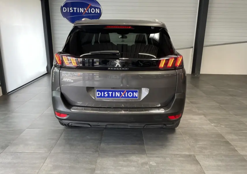 Vue arrière du Peugeot 5008 gris platinium 2024 avec feux LED 3D et logo Peugeot visible en intérieur showroom.