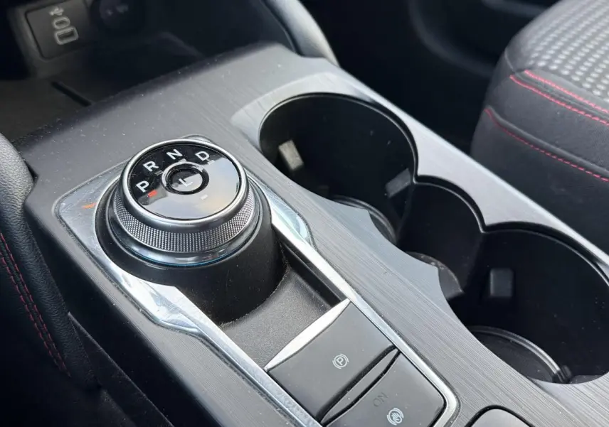 Gros plan sur la console centrale du Ford Kuga 2022 ST-Line, avec sélecteur rotatif de boîte auto et surpiqûres rouges sur sellerie noire.