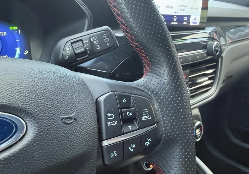 Gros plan sur le volant perforé noir avec surpiqûres rouges du Ford Kuga 2022, tableau de bord et commandes visibles.