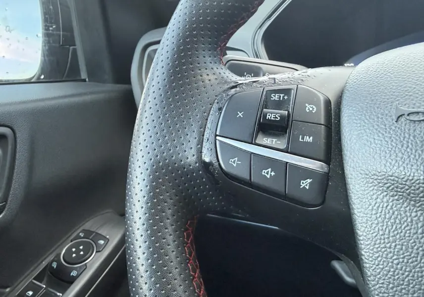 Gros plan sur le volant perforé noir avec surpiqûres rouges du Ford Kuga ST-Line 2022, côté gauche avec commandes intégrées.