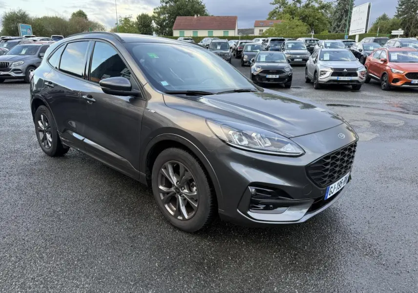 Ford Kuga gris métallisé en vue 3/4 avant droit, avec calandre et jantes alliage 18 pouces ST-Line visibles.